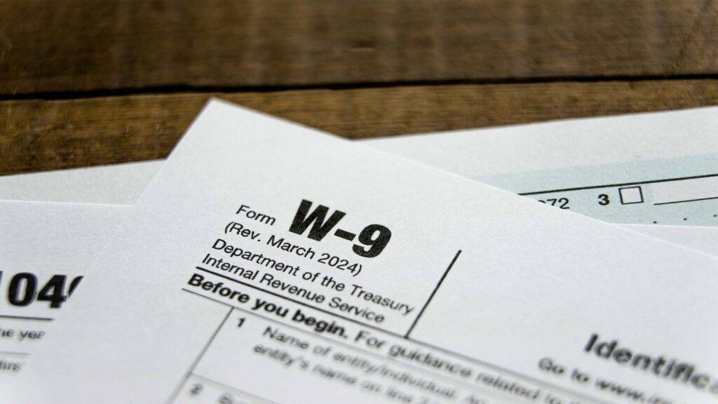 A W-9 tax form alongside an IRS instruction sheet is placed on a wooden table, indicating tax preparation activity.