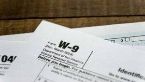 A W-9 tax form alongside an IRS instruction sheet is placed on a wooden table, indicating tax preparation activity.